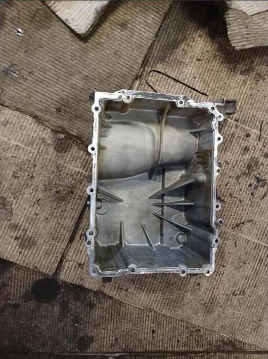 The aluminium sump pan removed from the car and photographed on the floor, cleaned out, its internal baffles and bolt holes visible.